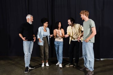 cheerful students talking and gesturing near art director in theater school