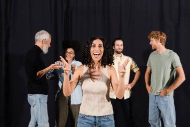 excited multiracial actress rehearsing near young actors and mature screenwriter in theater