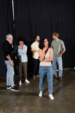 thoughtful multiracial actress looking away near multiethnic students and producer on background. Translation of tattoo: om, shanti, peace