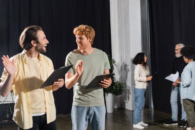 happy young actors with clipboards gesturing during rehearsal in acting skills school clipart