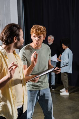young actors with clipboards grimacing and showing okay signs during rehearsal in acting school clipart