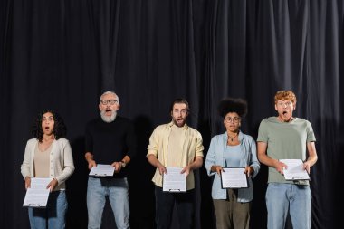 amazed multicultural actors with bearded art director holding clipboards during rehearsal in acting school clipart