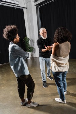 excited bearded producer gesturing and talking near multiethnic actresses in acting school clipart