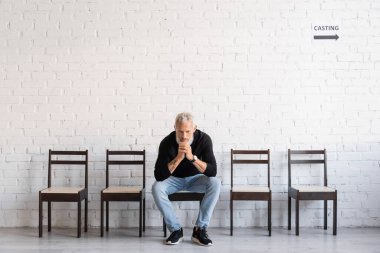 thoughtful man waiting for casting in theatre. Translation of tattoo: om, shanti, peace. You have to dig deep wells if you want to get clear water