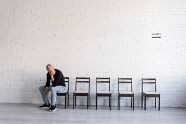 grey haired middle aged actor sitting on chair in corridor and waiting for casting