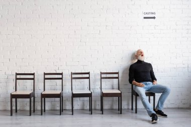 full length of mature man sleeping on chair while waiting for casting on chair near white wall