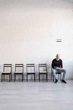 middle aged man in black turtleneck sitting on chair and reading screenplay while waiting for casting