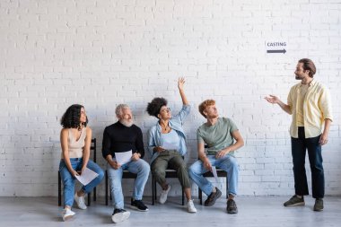 art director pointing at african american woman raising hand near multiracial actors waiting for casting 