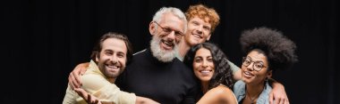 happy multicultural troupe embracing mature teacher of acting skills and smiling at camera, banner