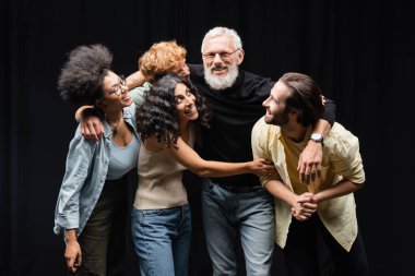 happy interracial actors hugging bearded grey haired art director in theater