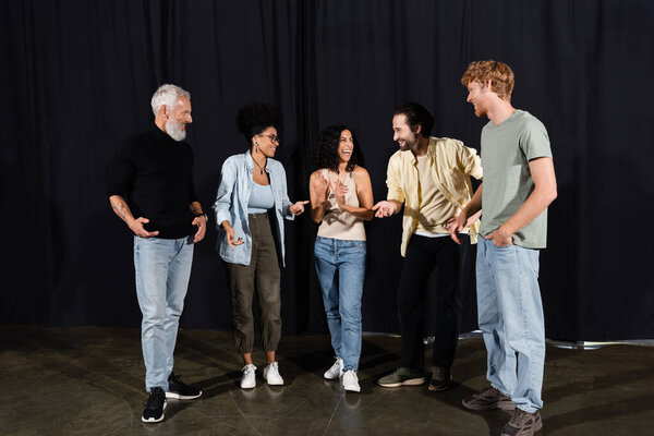 cheerful students talking and gesturing near art director in theater school