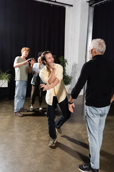 excited man rehearsing near middle aged producer and interracial actors talking on blurred background