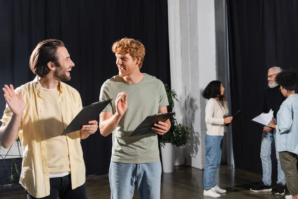 happy young actors with clipboards gesturing during rehearsal in acting skills school