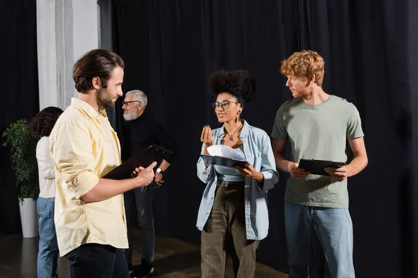 smiling african american woman with scenario talking to young actors in acting skills school