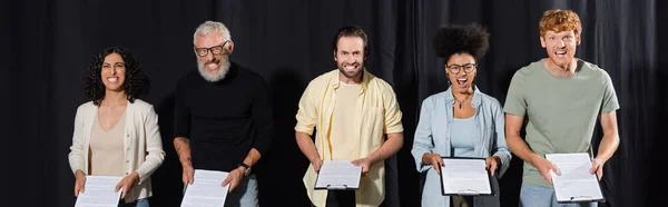 bearded art director with interracial students grimacing while holding screenplays, banner