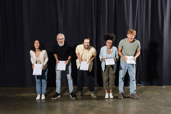 excited actors with bearded screenwriter looking at camera and laughing on stage in theater