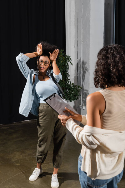 african american actress showing bunny ears with hands near multiracial woman with clipboard in theater