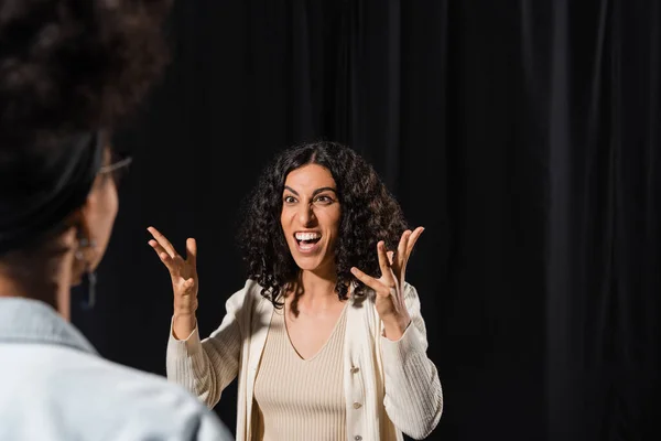 stock image multiracial woman gesturing and rehearsing with angry face expression near african american woman on blurred foreground