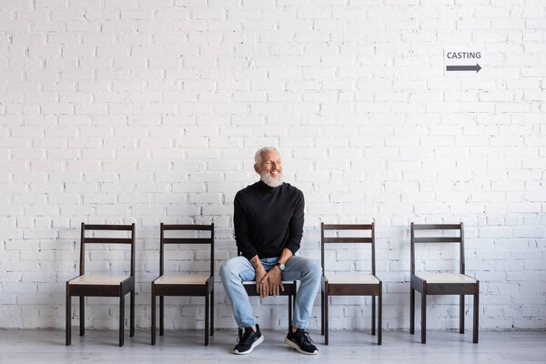 bearded man smiling with closed eyes while sitting on chair and waiting for casting