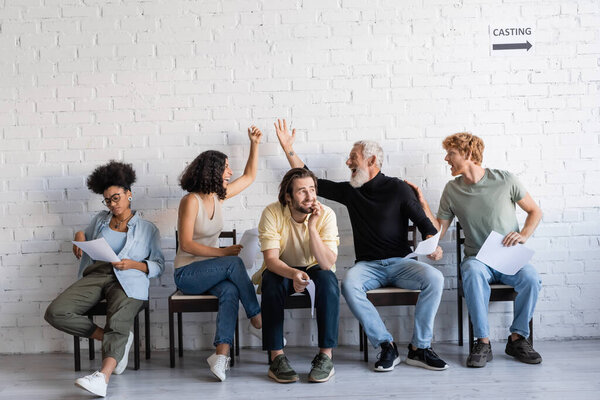 excited bearded man and multiracial woman showing success gesture near interracial actors. Translation of tattoo: kanji, danger