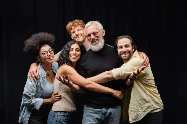 cheerful multiethnic actors embracing grey haired art director in theater