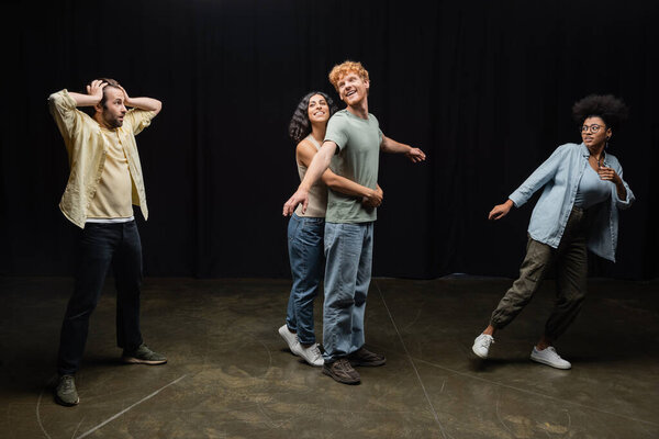 full length of emotional interracial students of acting skills school rehearsing in theater