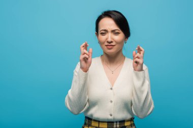 Young asian woman crossing fingers isolated on blue 