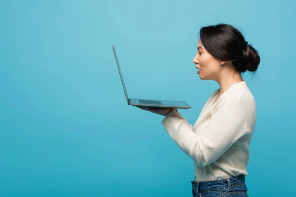 stock image Side view of asian freelancer holding laptop isolated on blue 