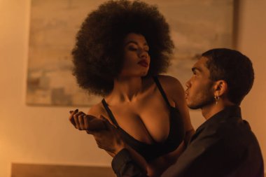 Genç adam, yatak odasında siyah sütyenli seksi Afrikalı Amerikalı kadının elini tutuyor.