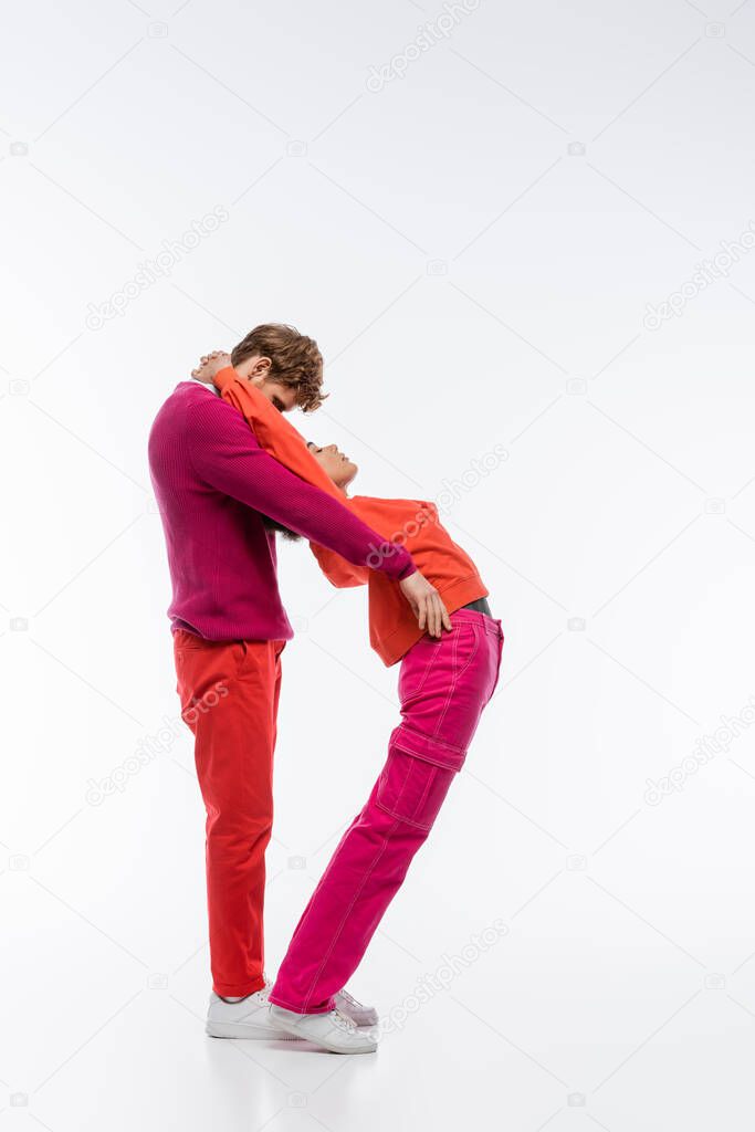 Side view of multiethnic couple in magenta color clothes showing d letter on white background