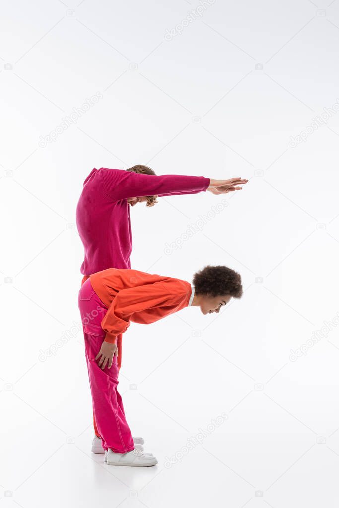 Side view of multiethnic couple in magenta color clothes showing f letter on white background
