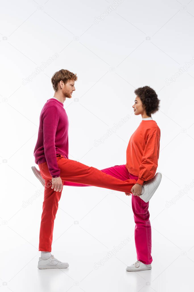 Side view of multiethnic couple in magenta color clothes showing h letter with legs on white background