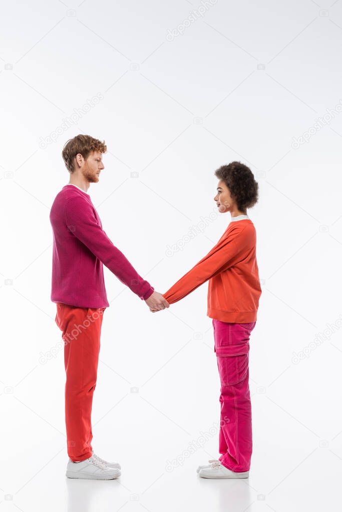 Side view of interracial couple in magenta color clothes showing m letter on white background