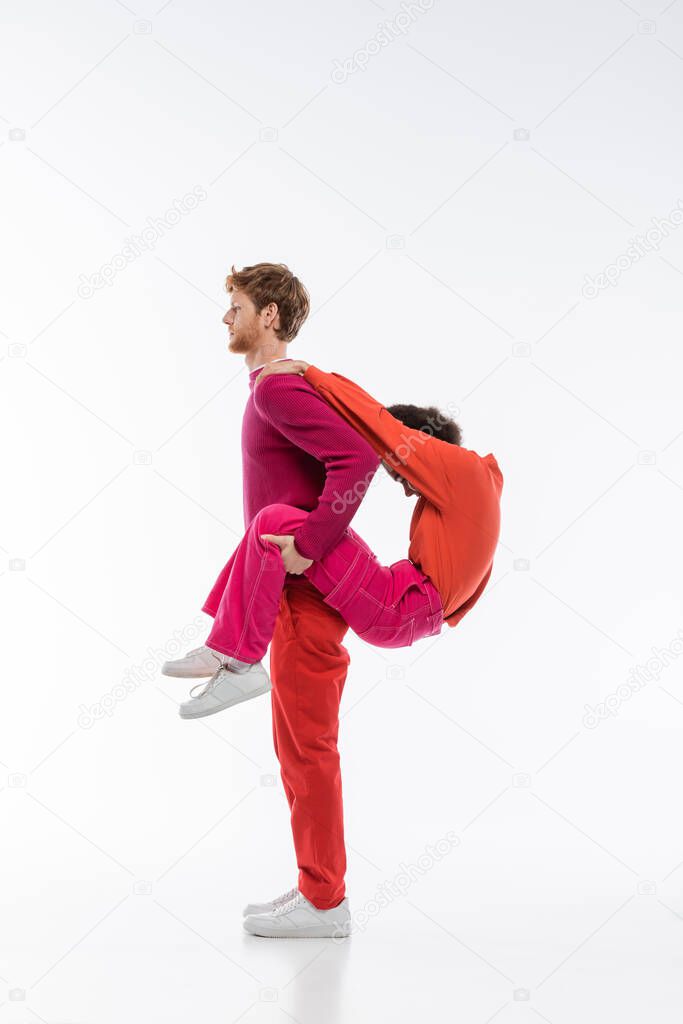 Side view of multiethnic couple in magenta color clothes showing p letter on white background