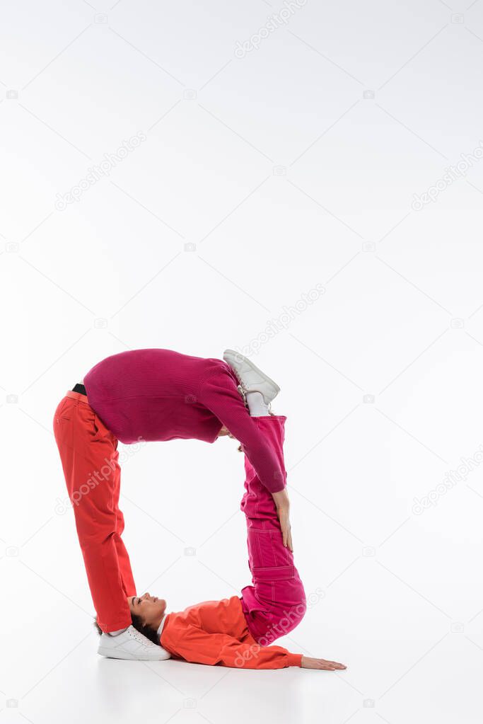 Side view of multiethnic couple in magenta color clothes showing q letter on white background