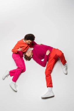 high angle view of happy redhead man hugging pleased african american woman in magenta color clothes lying on white  clipart