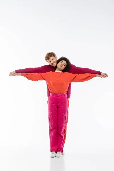 stock image happy and interracial couple in magenta color clothes showing t letter on white background 