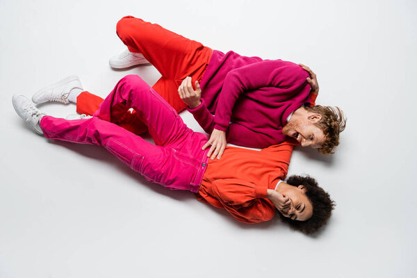 Вид сверху позитивного рыжеволосого мужчины, смотрящего на кудрявую африканскую женщину в платье цвета маджента на белом 