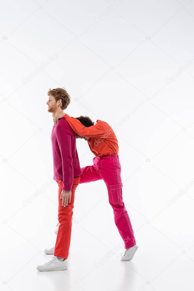 Side view of multiethnic couple in magenta color clothes showing R letter on white background