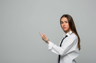 confused young woman in white shirt and tie pointing with finger isolated on grey clipart