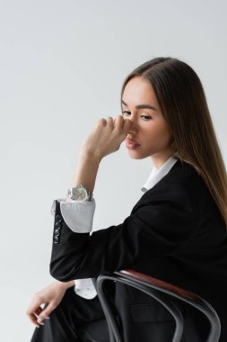 dreamy woman with long hair leaning on wooden chair back while looking away isolated on grey 