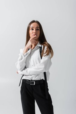 brunette young woman in black pants and suspenders posing isolated on grey 