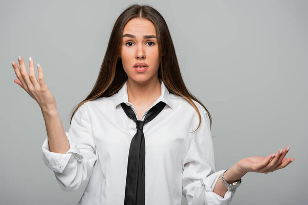 confused young woman in white shirt and tie gesturing isolated on grey