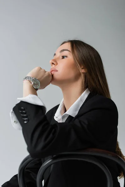 stock image pensive woman with long hair leaning on wooden chair back while looking away isolated on grey 