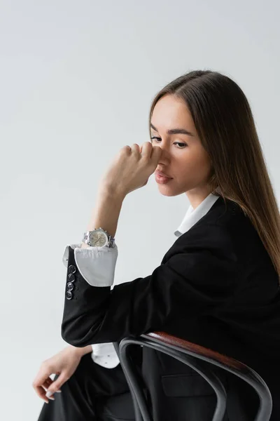 Stock image dreamy woman with long hair leaning on wooden chair back while looking away isolated on grey 