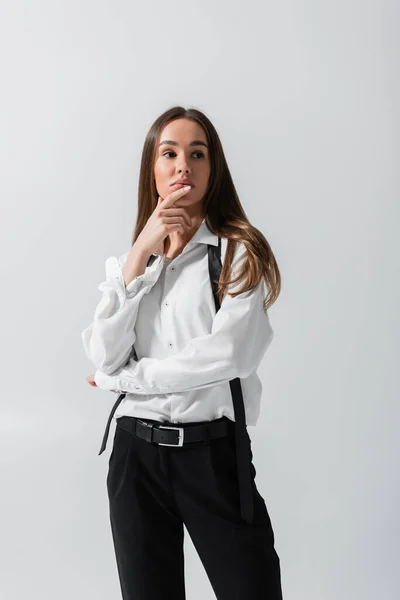 brunette young woman in black pants and suspenders posing isolated on grey