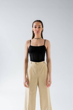 pretty model in beige pants and black top looking at camera isolated on grey 
