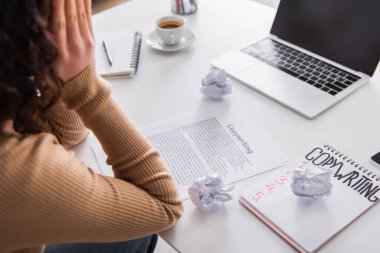 Cropped view of nervous copywriter sitting near papers and laptop at home  