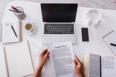 Top view of man holding papers with copywriting lettering near notebooks and devices at home 