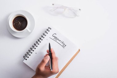 Top view of man holding pen near notebook with copywriting lettering and coffee on table 